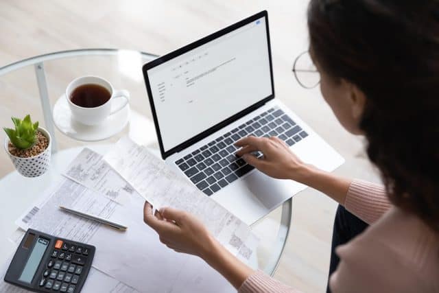 woman looking at receipt/paperwork while working on laptop