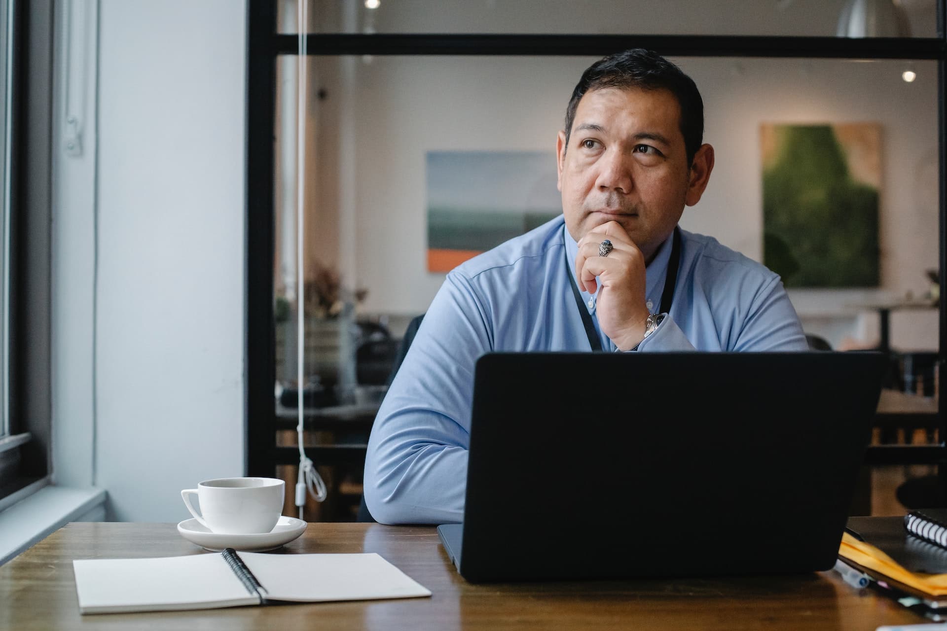 Thoughtful ethnic businessman using laptop while working in office.