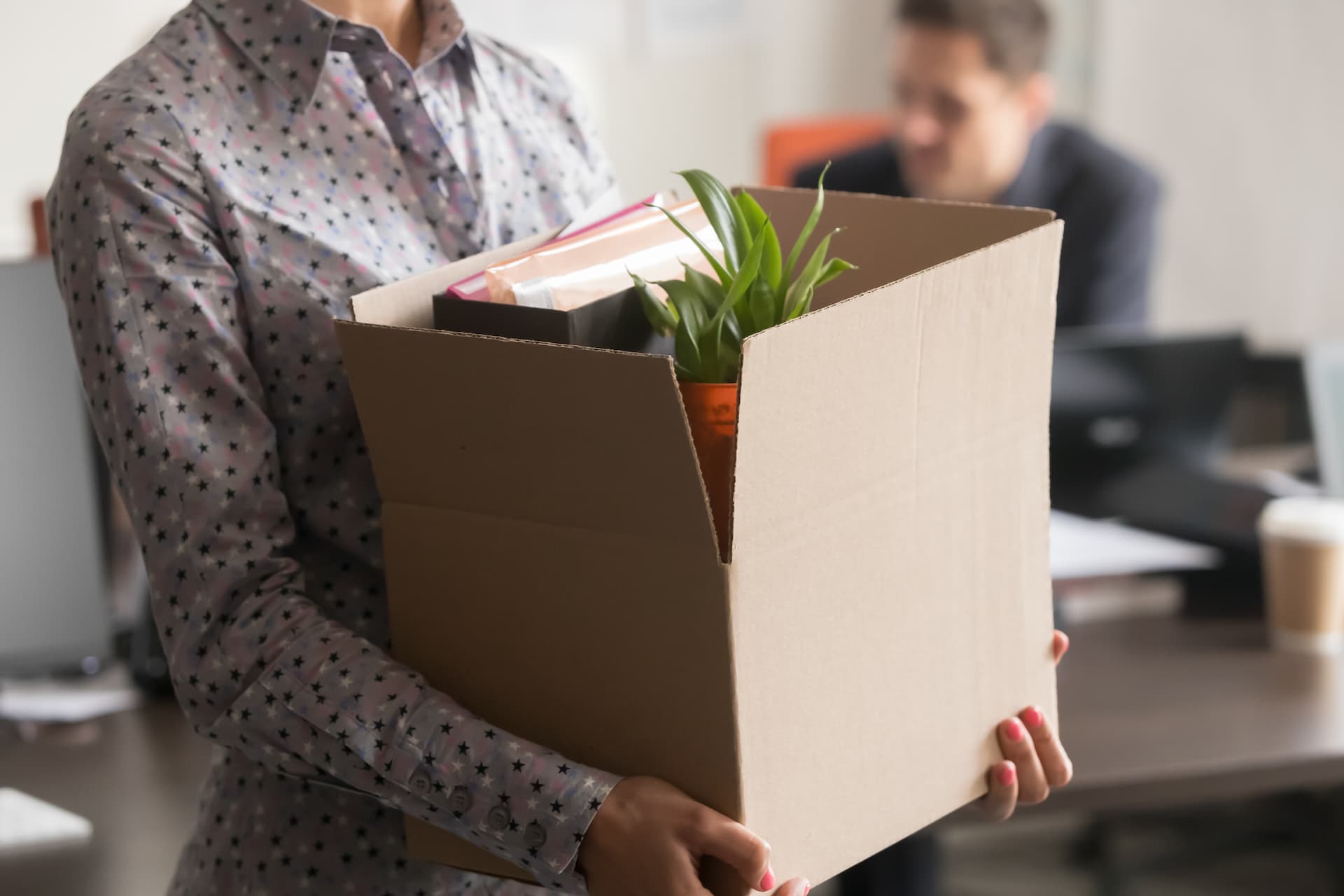 Close up view of a female employee holding cardboard box with her belongings leaving the office.