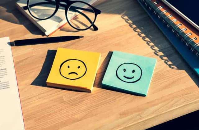 Two stacks of post it notes laying on a desk, one with a happy face and one with a sad face.