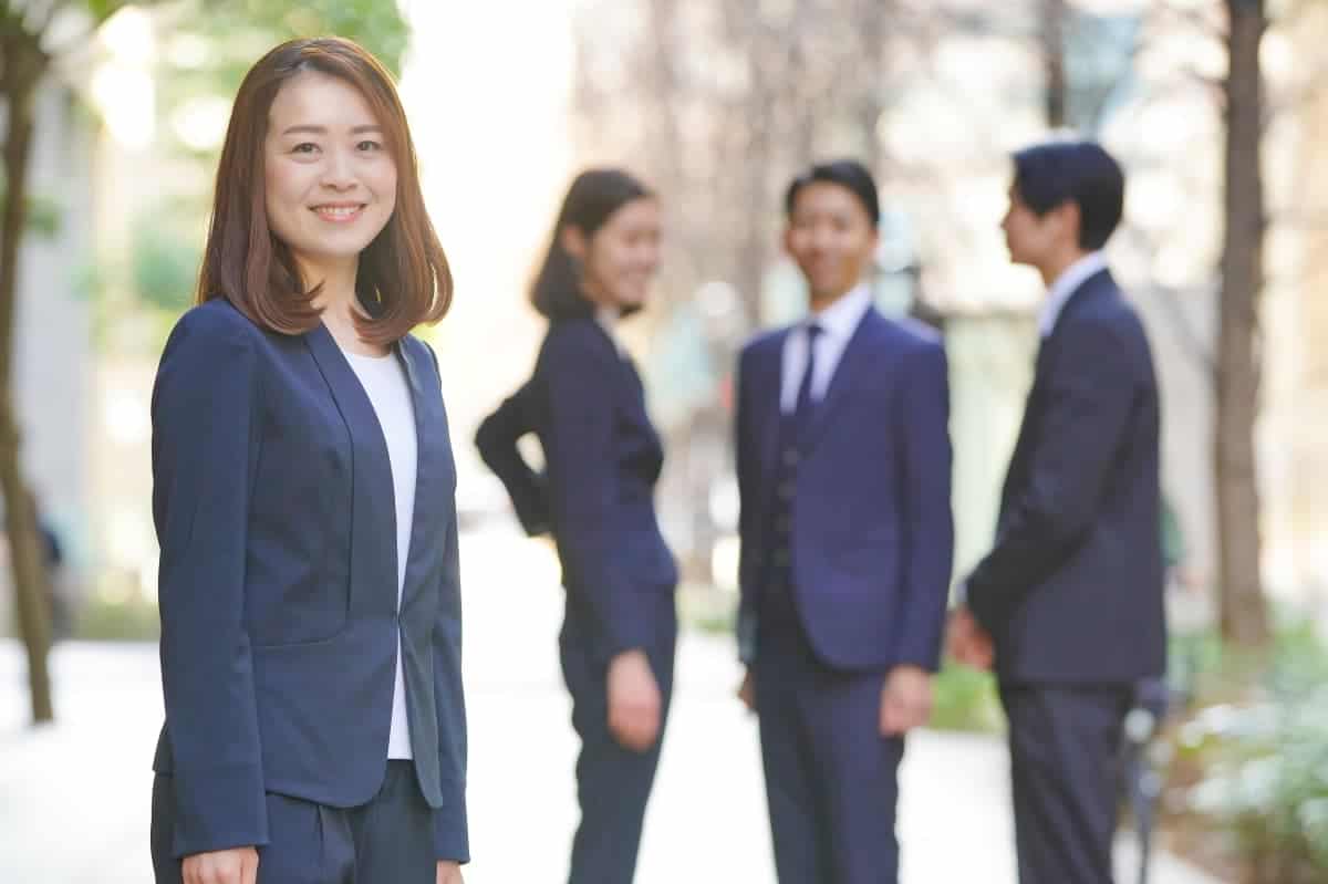 Smiling, successful business woman standing in the foreground with three colleagues happily engrossed in discussion in the background.