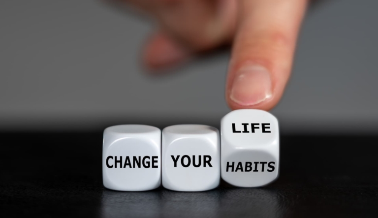 Three rolling dice. The first has the word 'change', the second, 'your', and the third is being moved from one surface with the word, 'habits' to another one with the word 'life'.