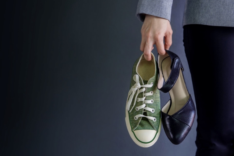 Woman holding her converse shoes and high heels in one hand.