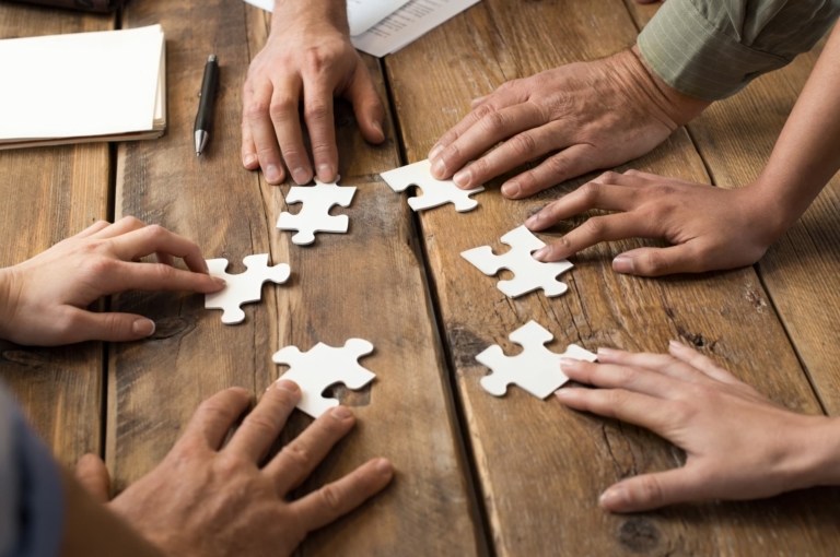 Closeup of businessman and woman putting jigsaw puzzle pieces together on a desk, collaboratively.