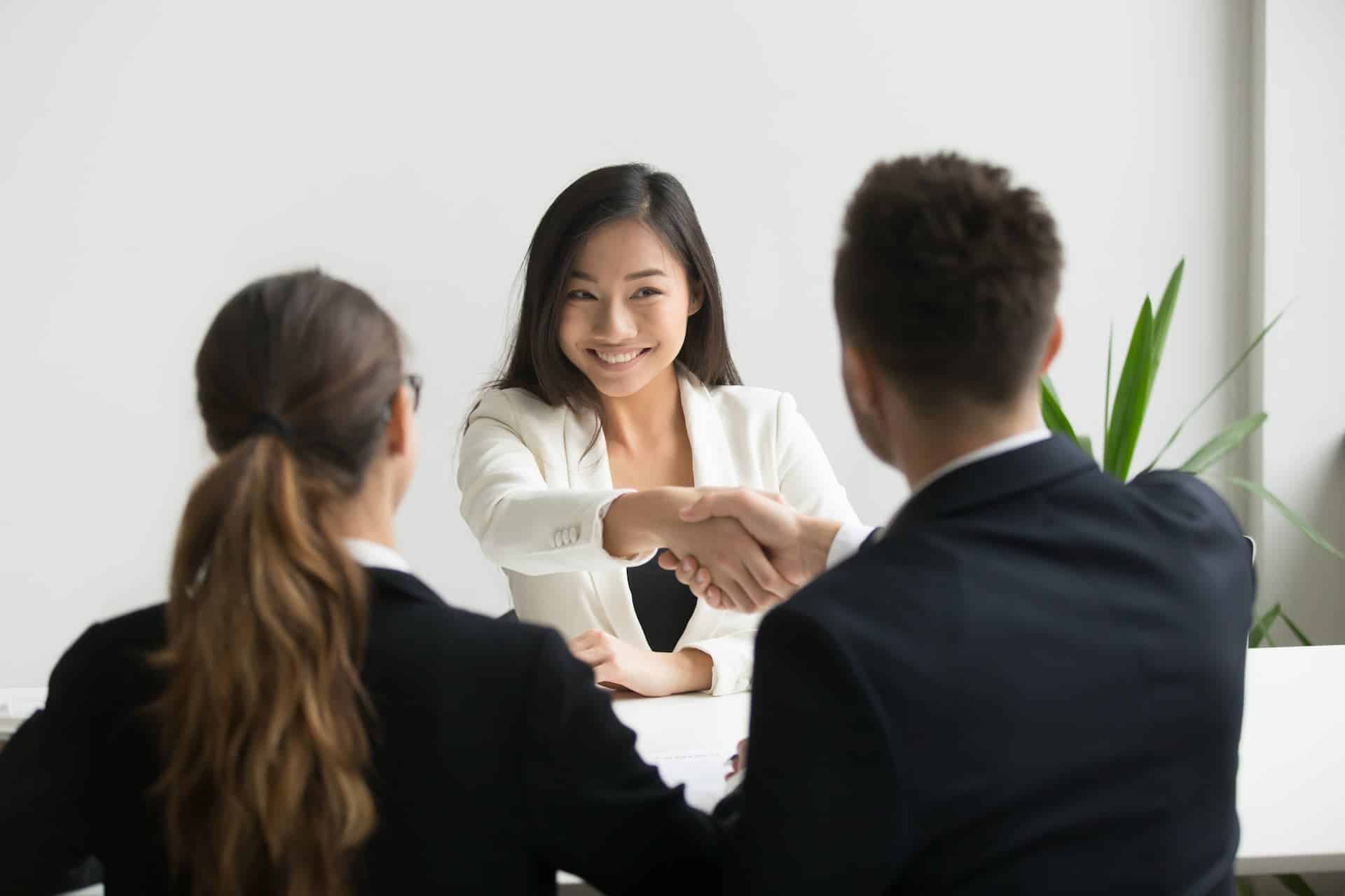 Interviewers shaking the hand of the interviewee, signaling that she's hired.
