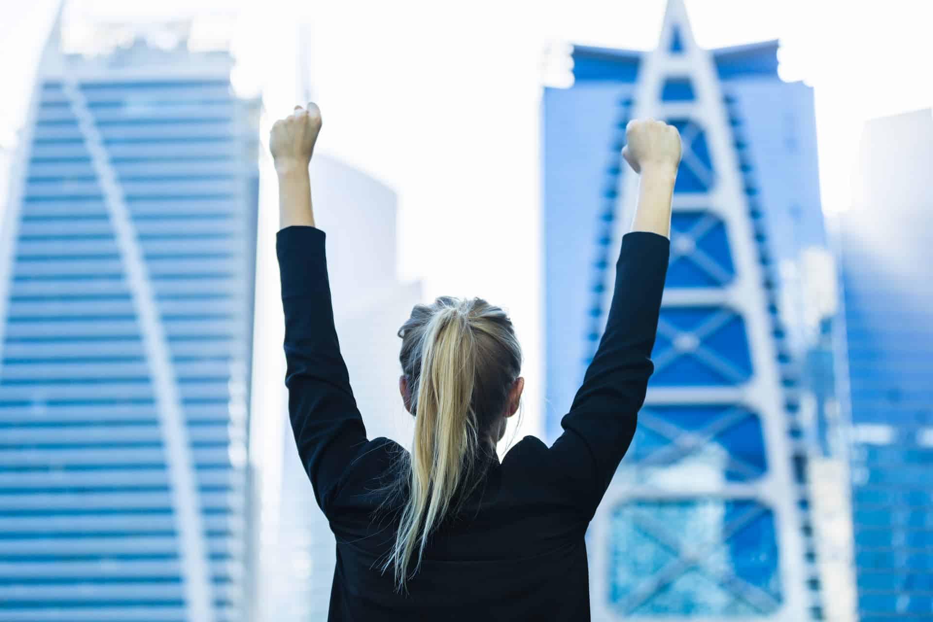 A woman in a city with her hands up in a celebratory pose.