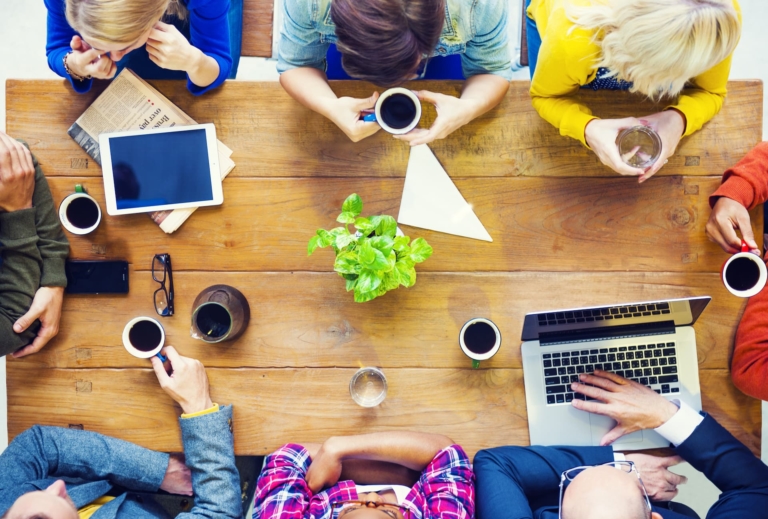 Bird's-eye view of a café meeting with people sitting at a wooden table, drinking coffee while they discuss ideas.