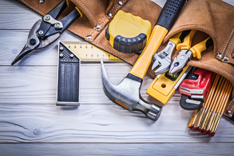 Leather tool belt filled with construction tools resting on a wooden board.
