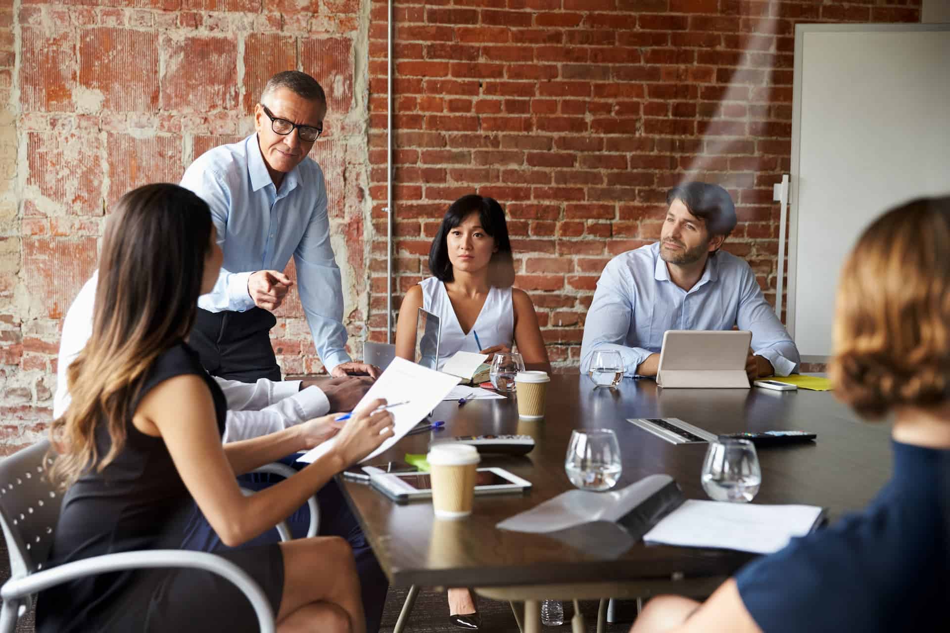 Businesspeople in a modern boardroom with exposed brick walls engaged in a meeting.