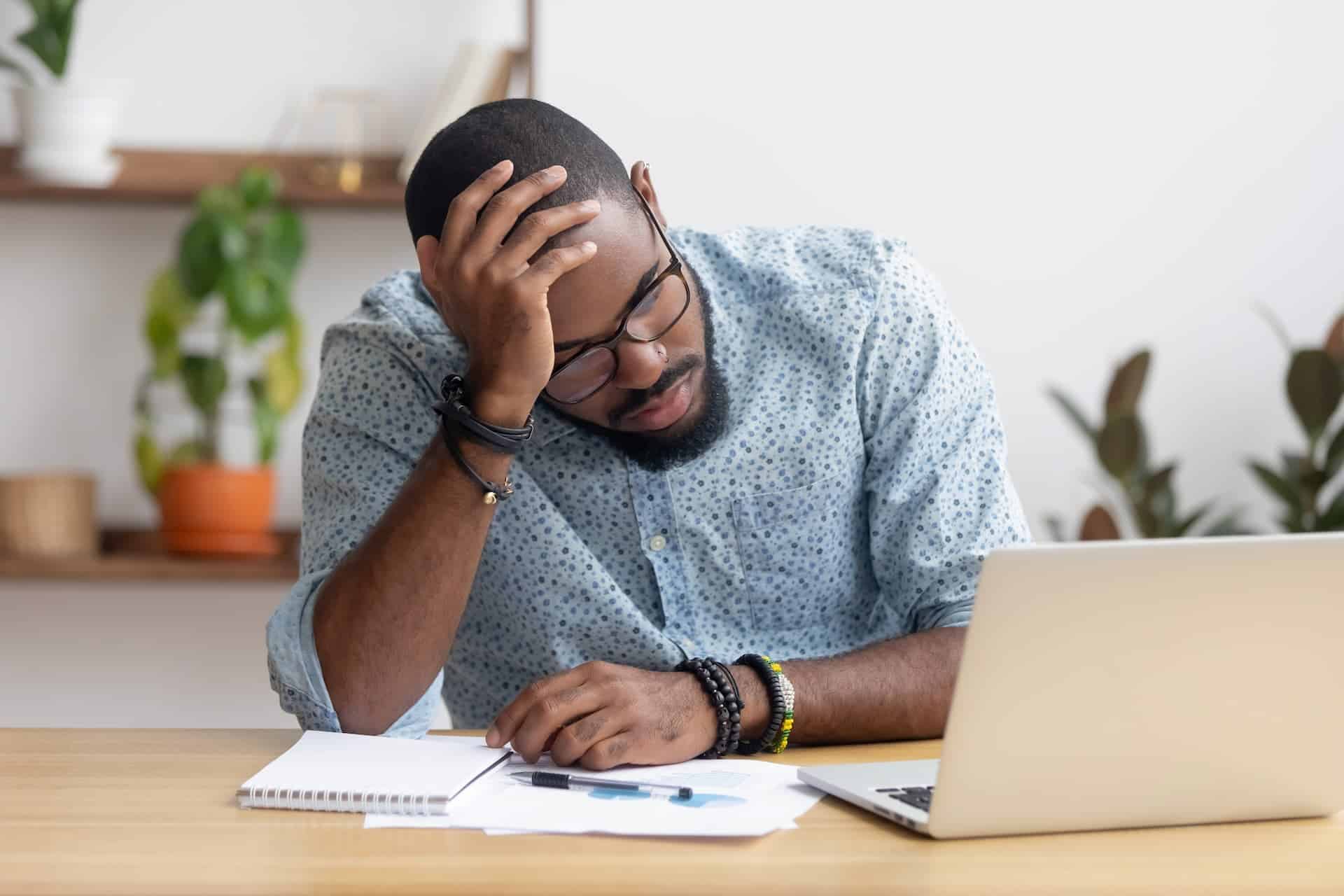 Man working looking at his laptop with his hand on his forehead feeling exhausted and regretful.
