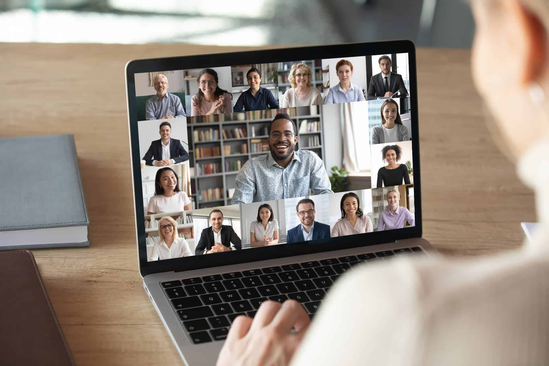 Female employee engaged in a video call, focused on her laptop screen displaying multiple participants in a virtual meeting.