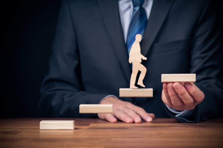 Businessman in a tailored suit holding a wooden staircase of growth and development, embodying the concept of coaching.