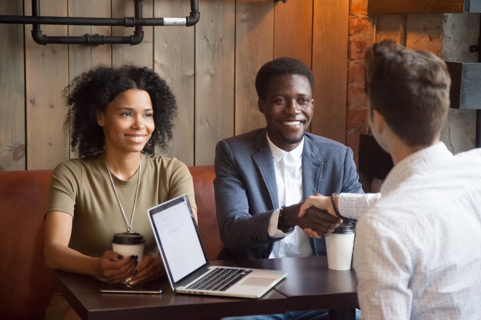 A couple smiling as they shake hands with a professional at a café meeting, illustrating the power of networking for introverts.