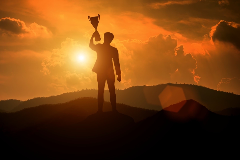 A silhouette of a businessman holding a trophy against a vibrant sunset backdrop, symbolizing motivation and achievement.