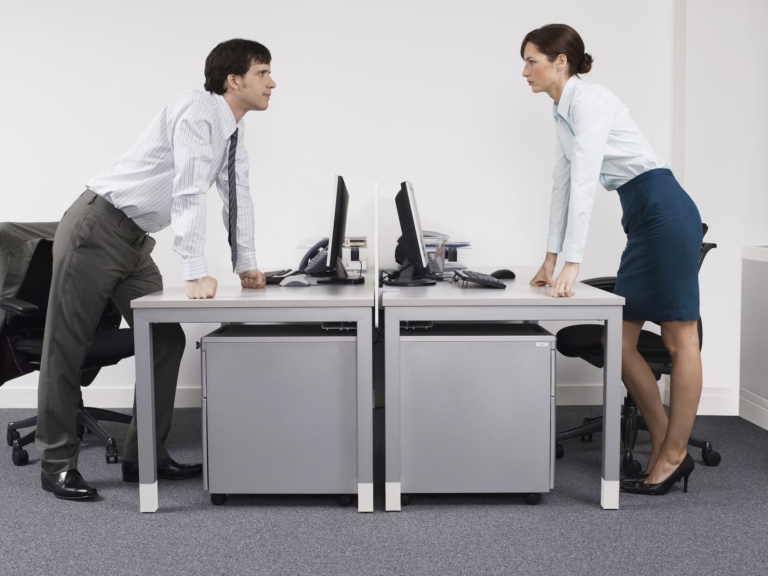 Two employees, one male and one female, stand facing each other across desks in a competitive stance, reflecting the dynamics of office politics and the pursuit of climbing the corporate ladder.