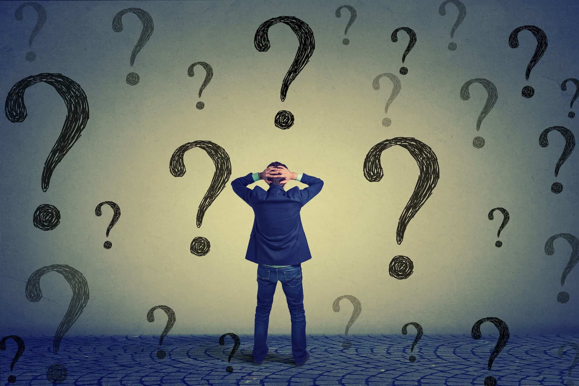 A man contemplating decisions in front of question-mark-covered wall.
