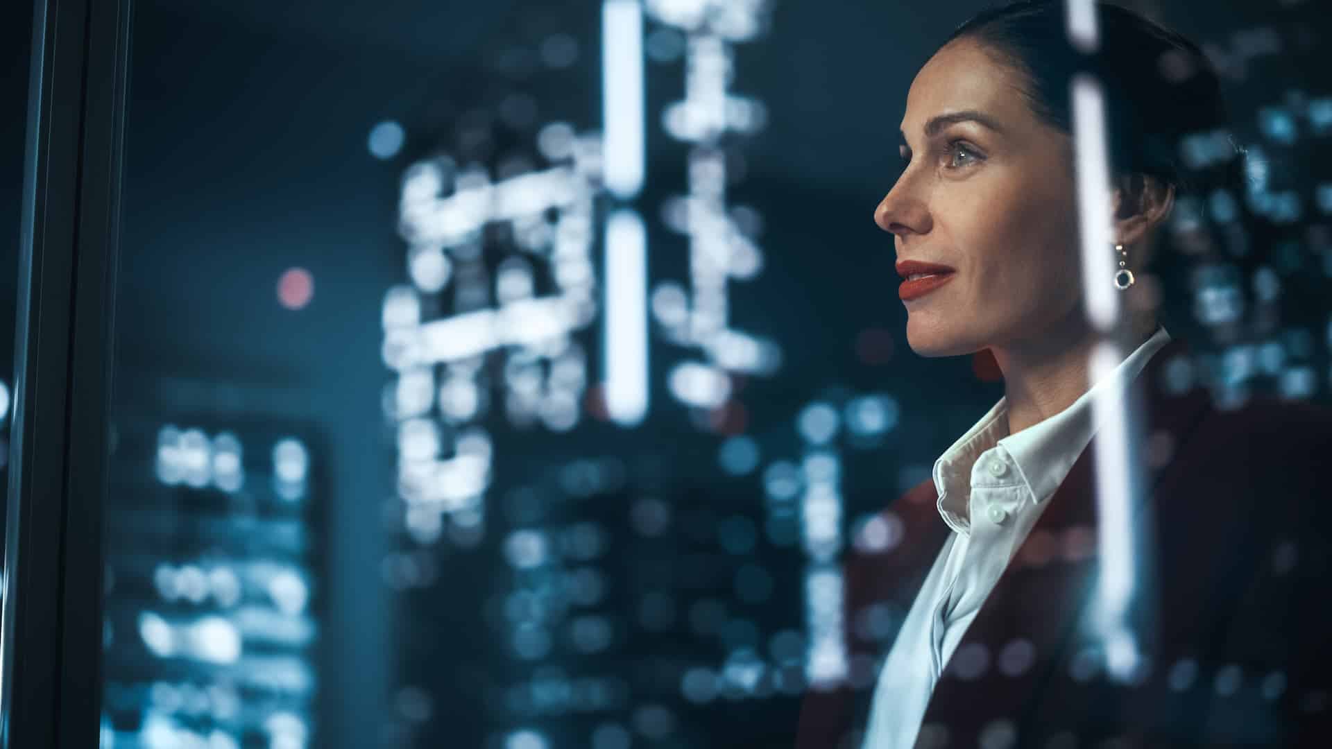 Businesswoman looking out office window, gazing at city lights with a look of inspiration and motivation.