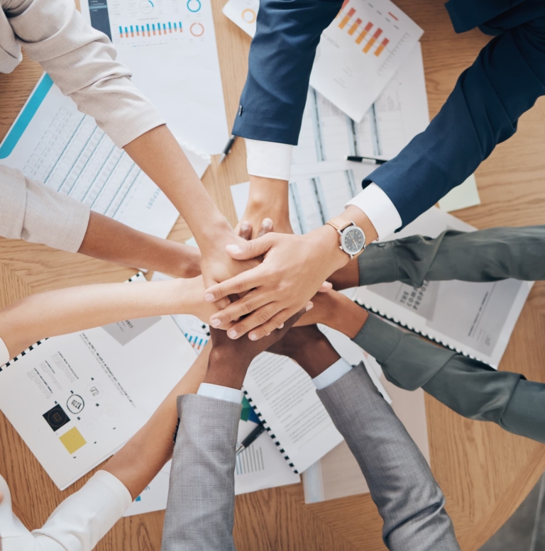 Hands joined together over a desk, symbolizing a culture of collaborative teamwork.