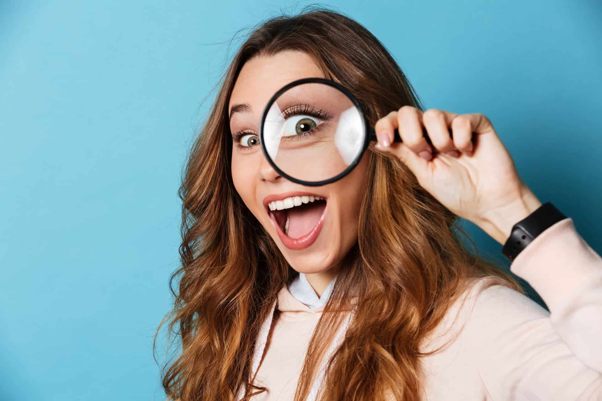 A woman holding a magnifying glass to her eye, showcasing the value of curiosity and discovery.