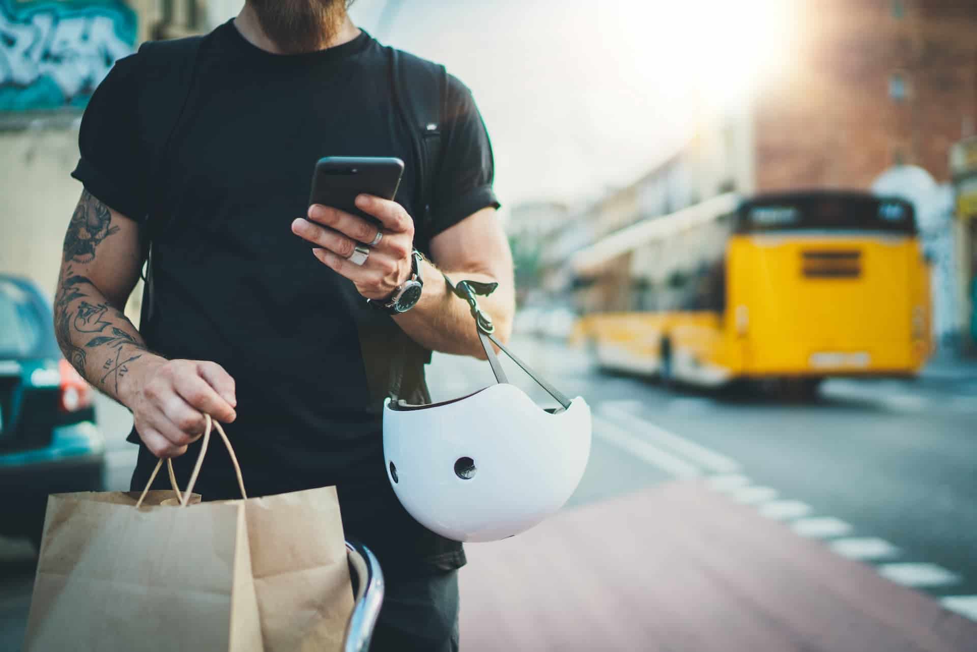 A man's arms carrying a helmet, a phone, and a food bag, symbolizing the gig economy and the diverse range of tasks and services it encompasses.