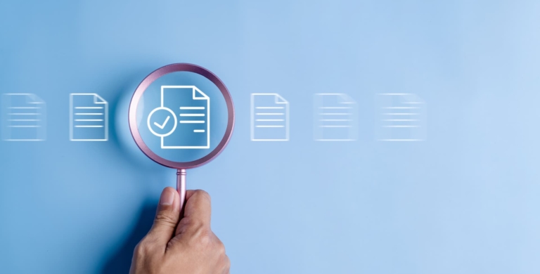 A hand holding a magnifying glass over various job search icons, symbolizing the detailed search for job opportunities.