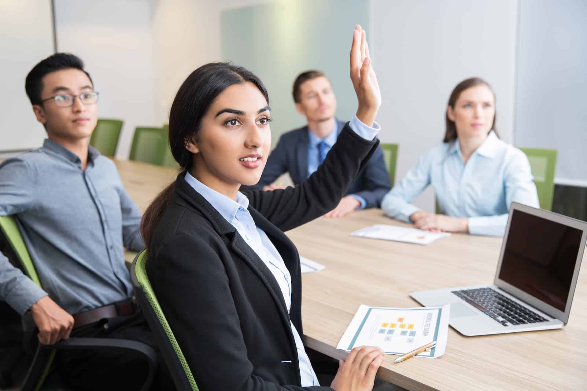 Woman with her hand raised in a meeting, symbolizing the courage to speak up.