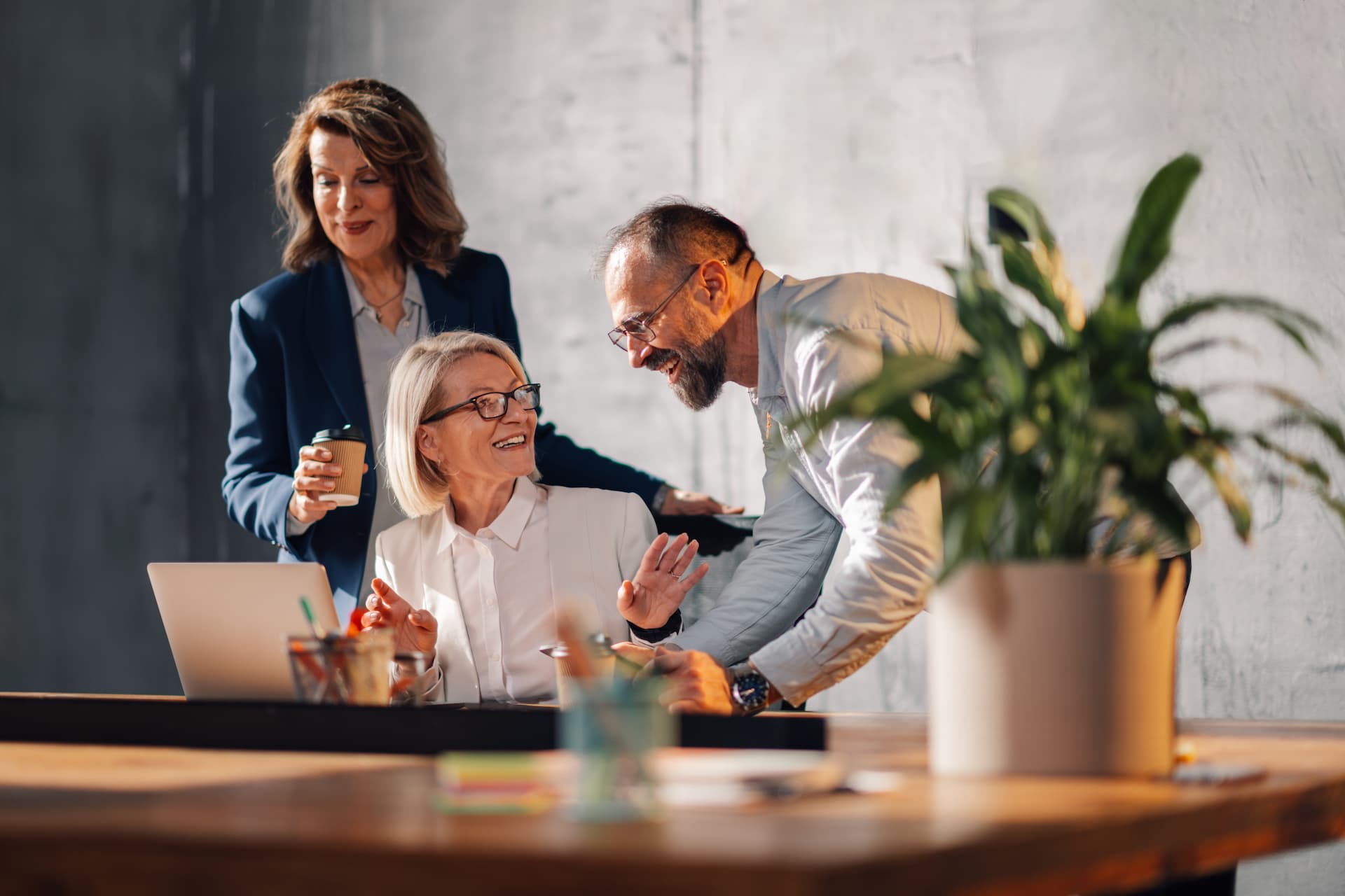 Three workers in an office collaborating on a laptop, illustrating how companies and HR professionals can invest in their employees to foster professional growth.