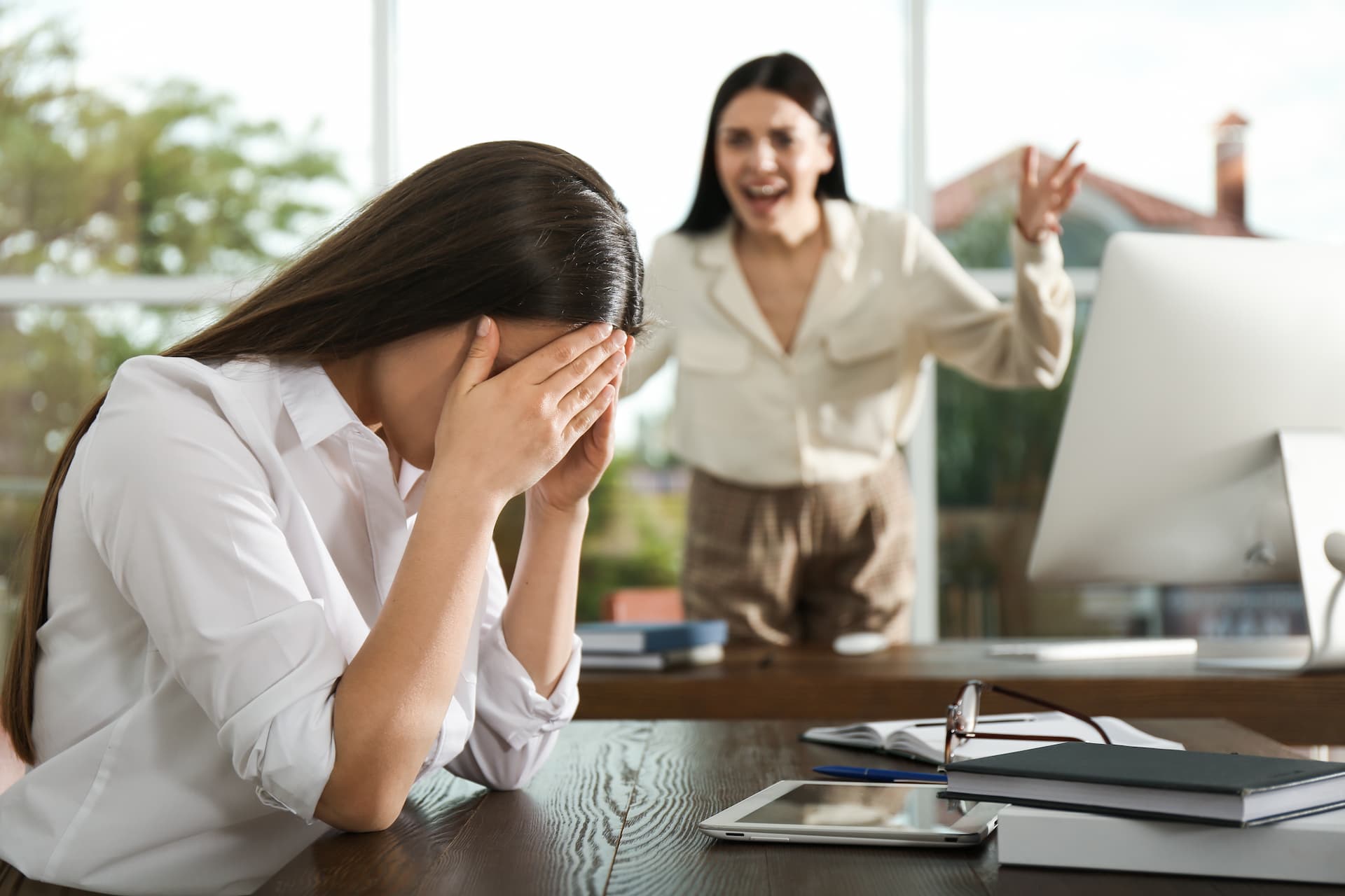 Woman in an office yelling at another woman who has her hands over her face, appearing to cry, showcasing a toxic work environment.