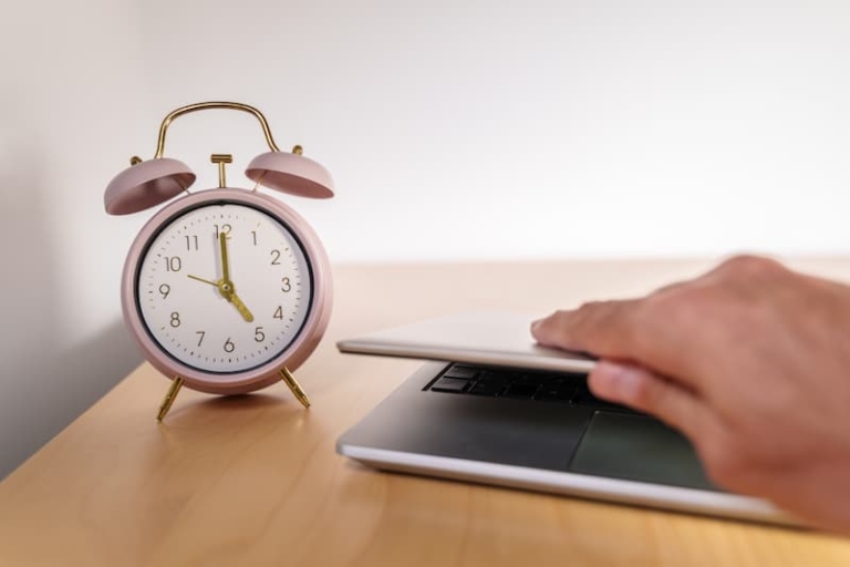 A clock showing 5 PM and a hand closing a laptop showcasing the end of the workday and the importance of work-life balance and setting boundaries.