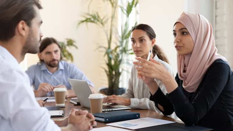 A diverse group of workers gathered around a table, engaged in a problem-solving discussion, exchanging ideas and strategizing together to find solutions, highlighting teamwork and diversity in problem-solving efforts.