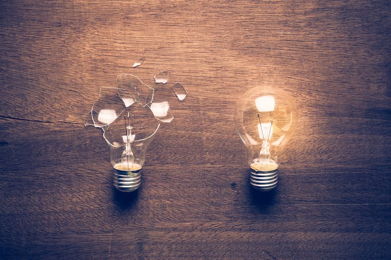 A broken lightbulb beside a glowing, functional lightbulb, symbolizing the concept of learning from failure and success in innovation and experimentation.