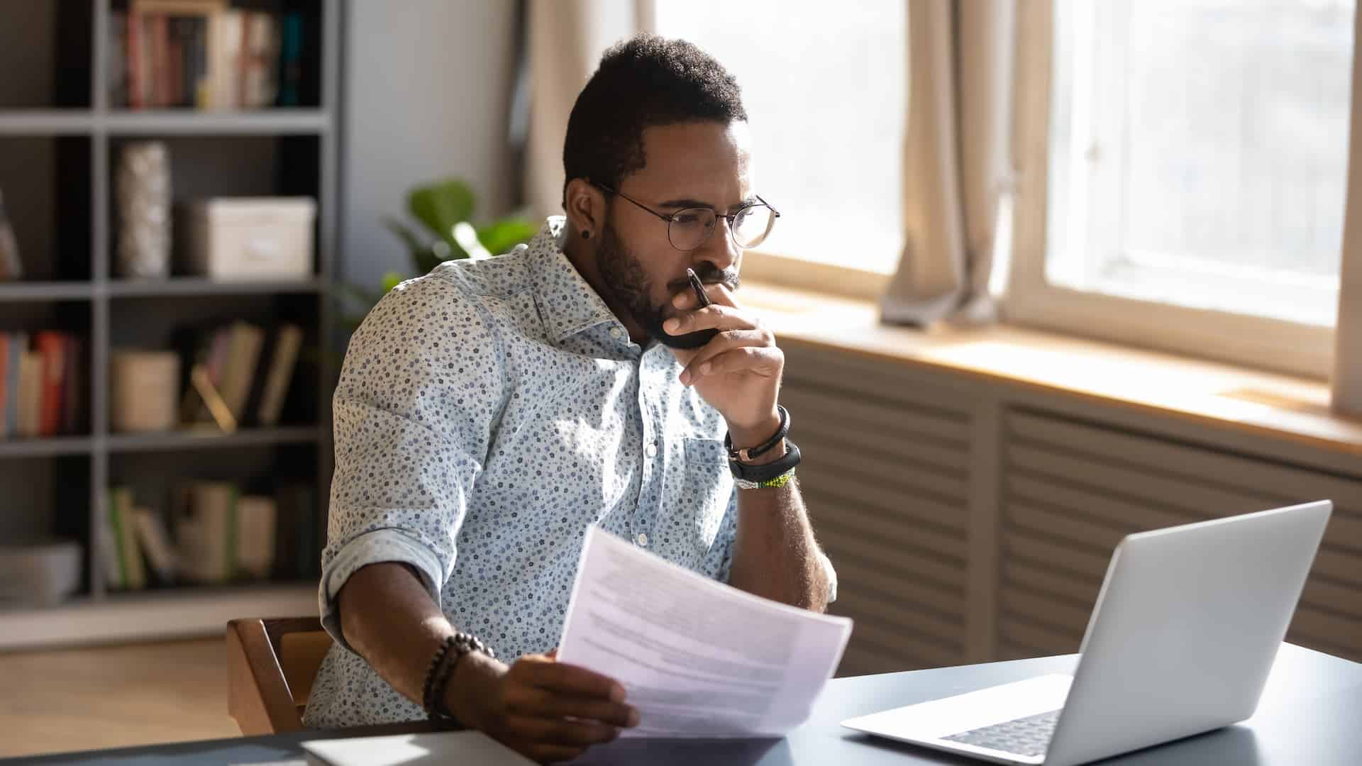Man thoughtfully looking at his laptop, with a focused expression, indicating he is engaged in critical thinking.