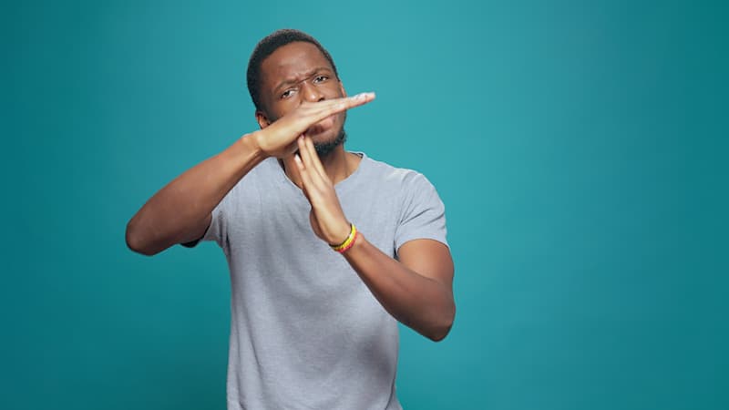 A man with his arms raised in a perpendicular gesture, asking for a time-out, symbolizing the importance of setting work boundaries.