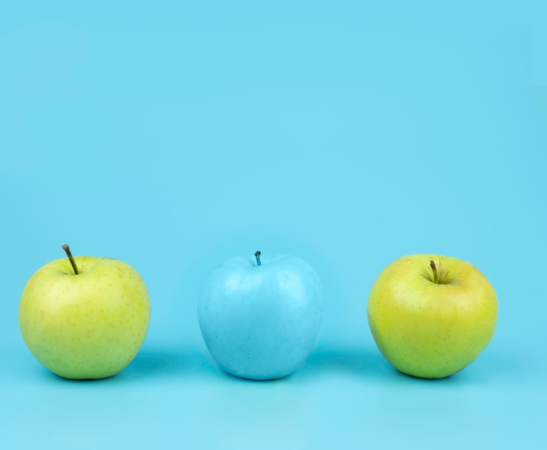 Two green apples and a middle blue one that matches the background color, symbolizing adaptability and the ability to adjust and fit into different contexts.