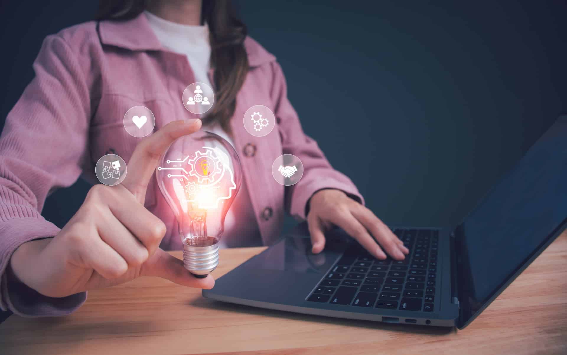 A woman working on her laptop in her office, gently touching a glowing lightbulb with her finger, symbolizing a moment of inspiration and creative adaptability.