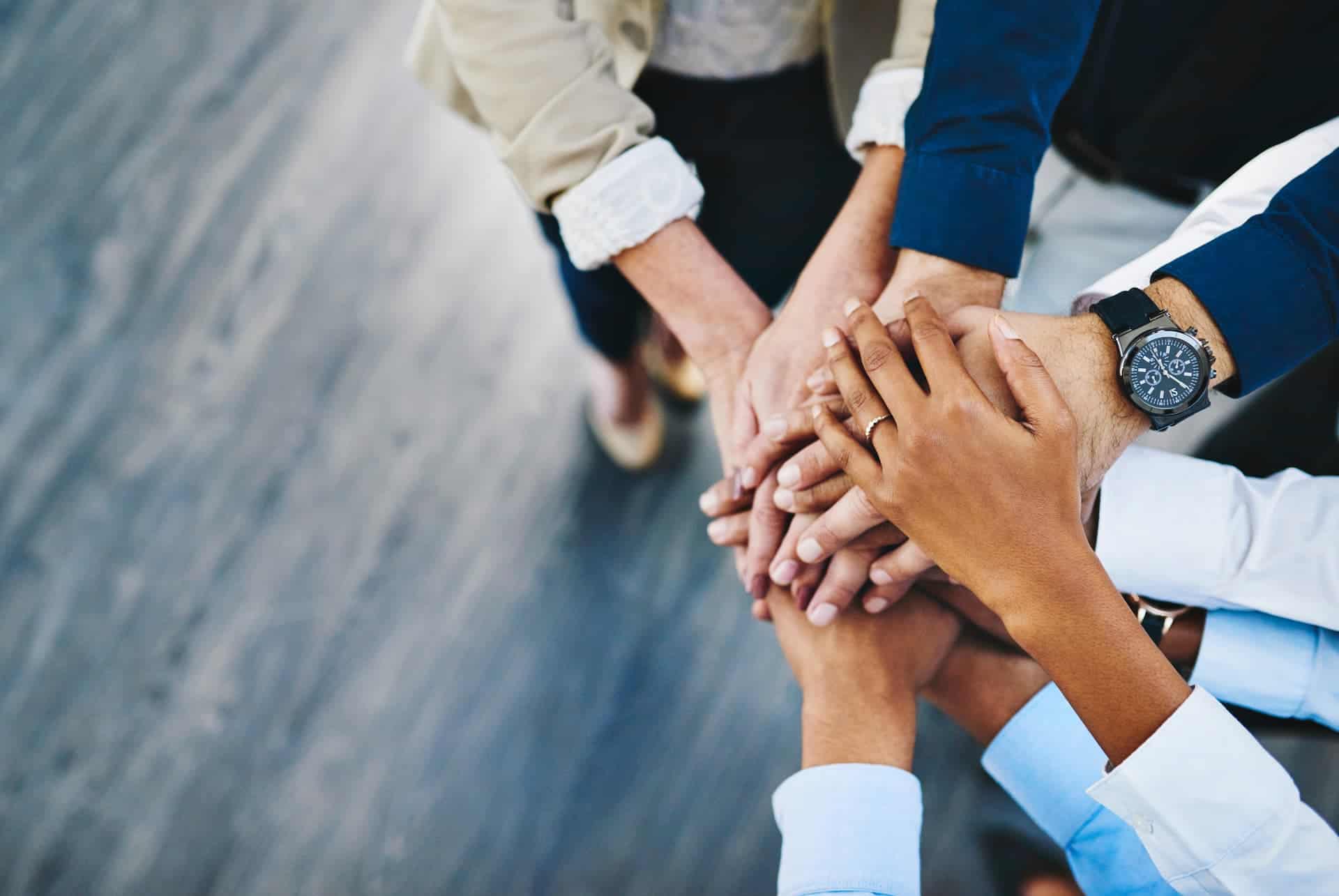 A group of hands gathered together in an office, symbolizing teamwork and confidence in their collective efforts.