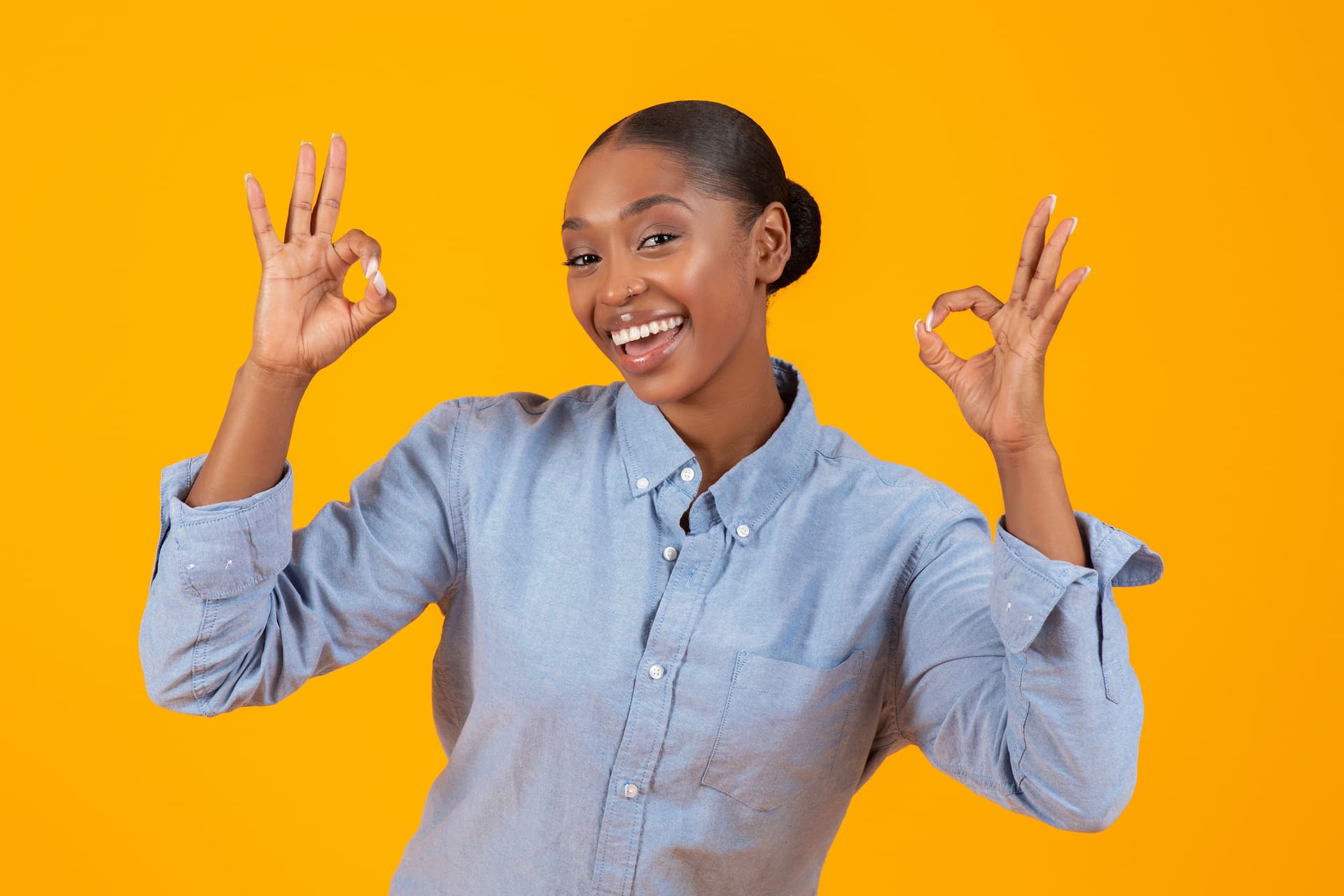 A professional woman in work attire is smiling and holding both hands up with an 'OK' finger gesture, illustrating the concept of giving feedback.