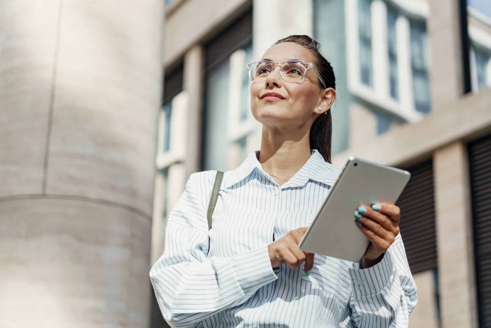 A professional woman confidently walking in a city, holding a tablet, embodying the forward-thinking, visionary leadership that defines a lasting career legacy.