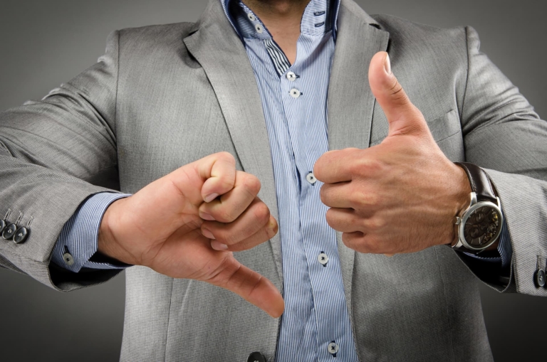 A close-up of a man's hands, with one hand giving a thumbs-up and the other giving a thumbs-down -- gestures and body language cues.