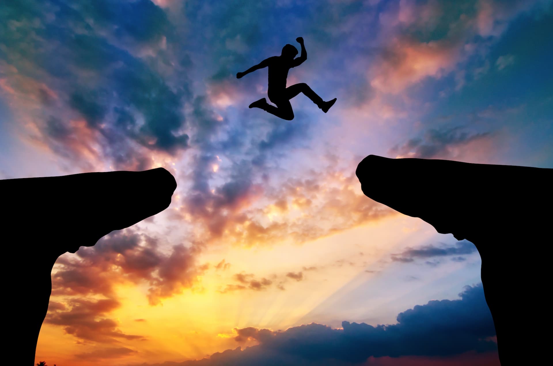 Silhouette of a person leaping between two cliffs against a colorful sunset sky, capturing the essence of bold decision making.