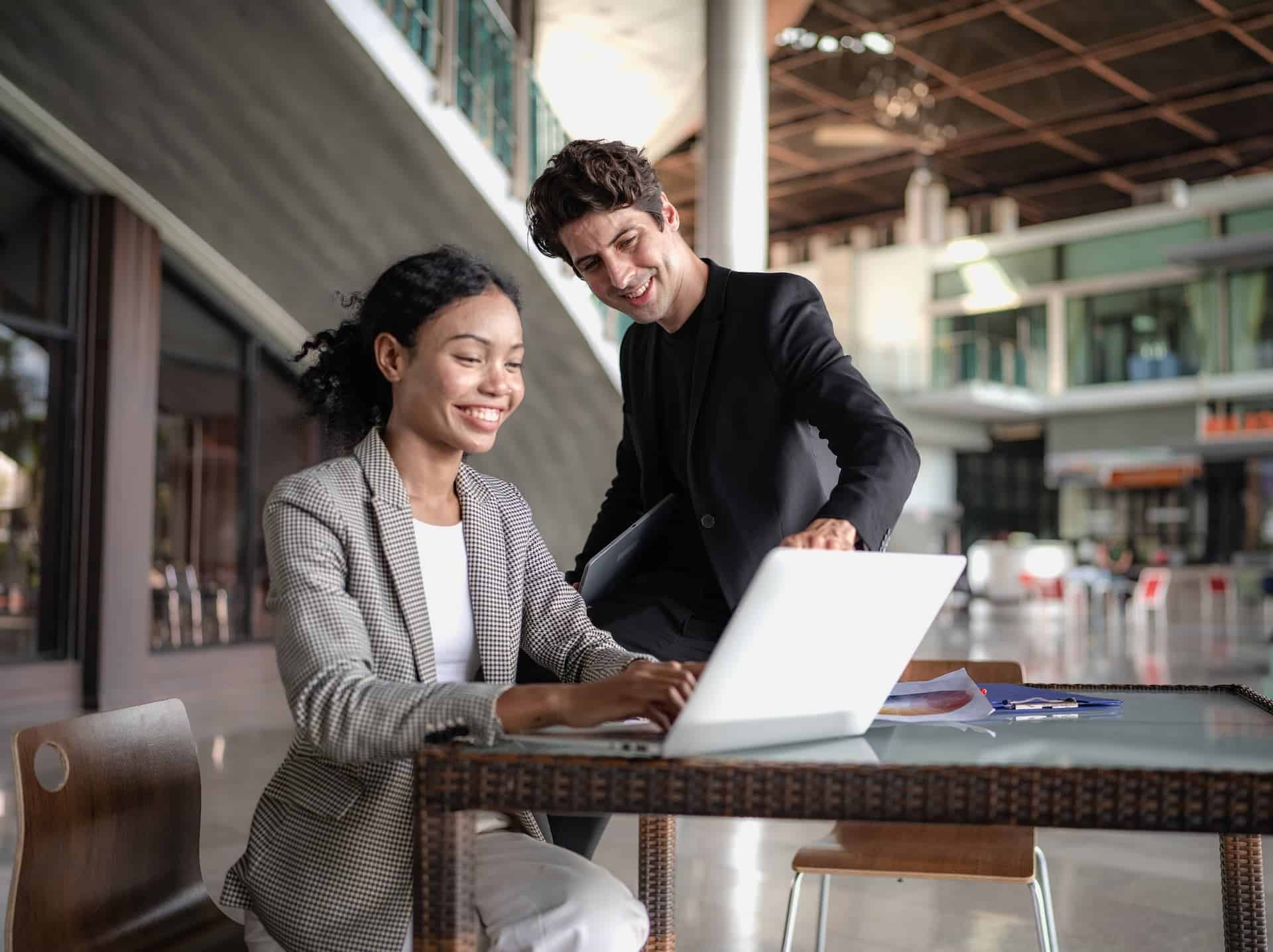 A woman working while a man looks at her computer screen, showing the pragmatic balance between teamwork and individual effort.