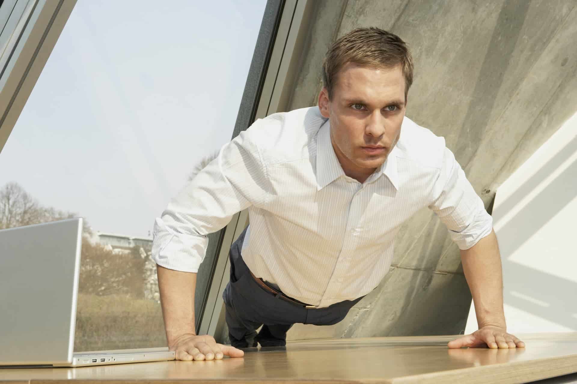 A man intensely performing push-ups with a laptop open beside him, symbolizing determination and focus as part of his deliberate practice routine.