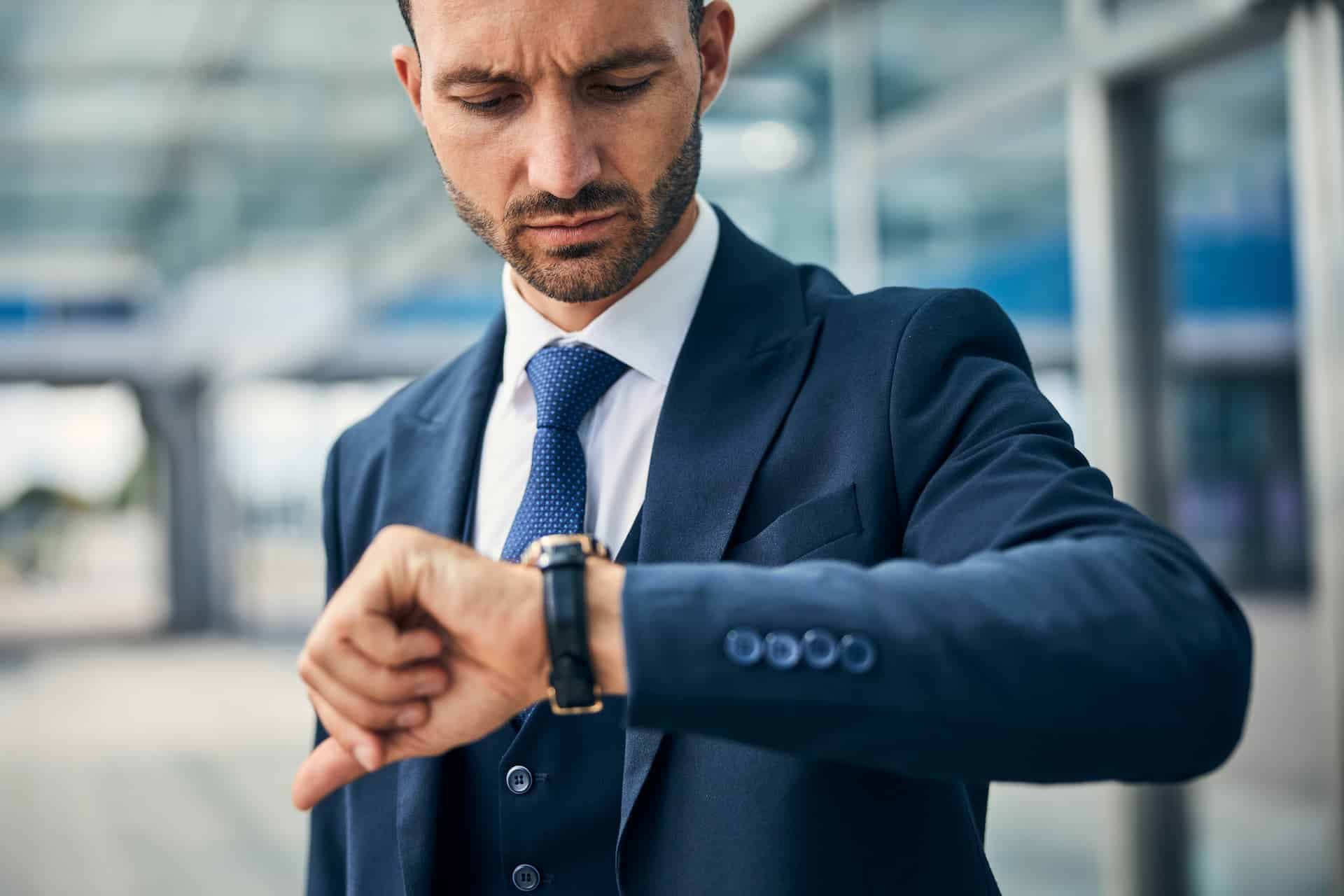 A manager in a suit glancing at his watch, representing the pragmatic need for time management and prioritization in a fast-paced professional setting.