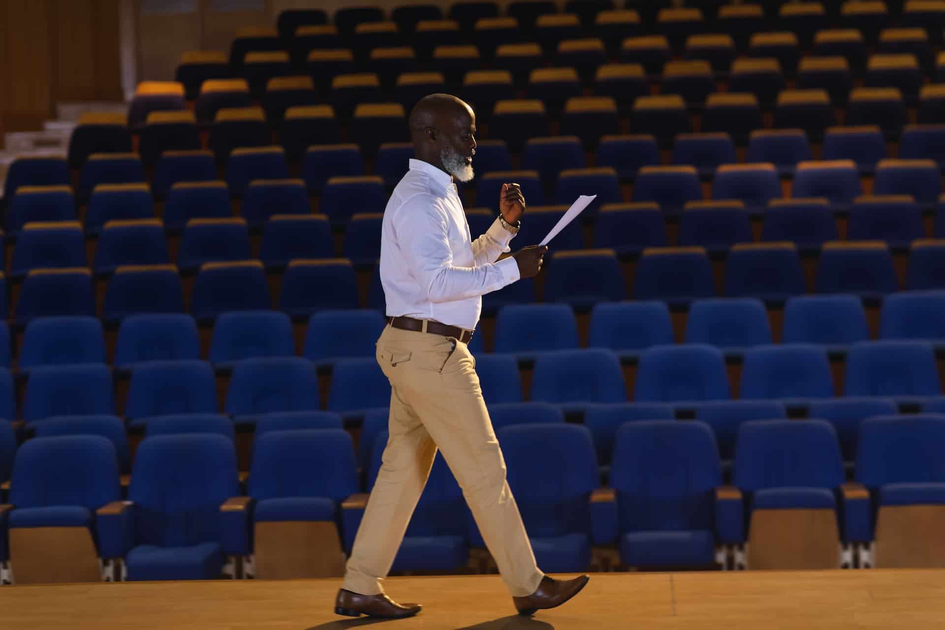 A man standing and gesturing, practicing his presentation in front of an imaginary audience, focusing on refining his delivery as part of deliberate practice.