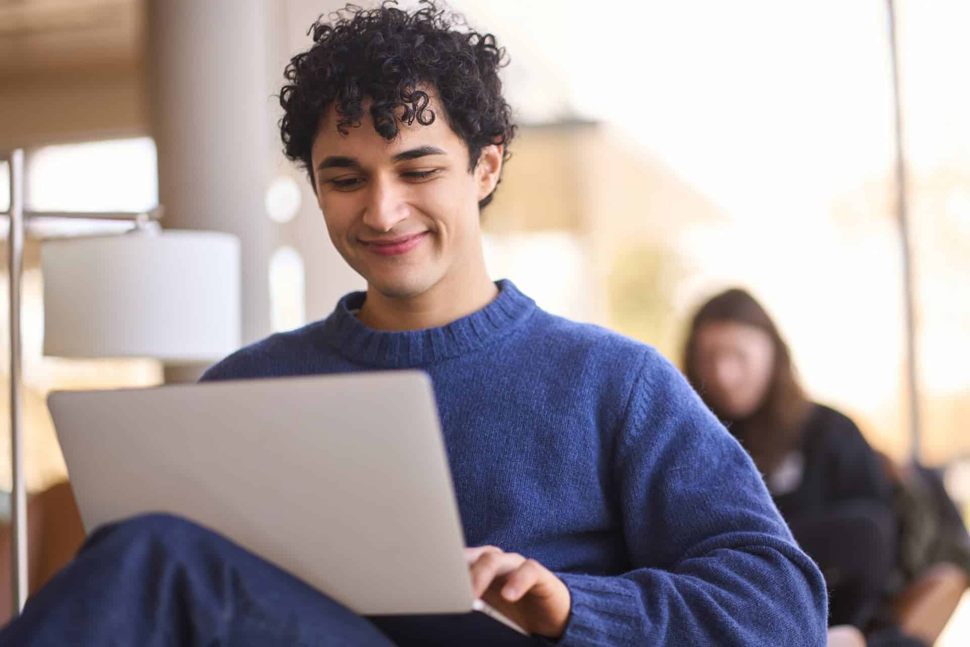 A smiling man working with a laptop on his legs, reflecting a sense of satisfaction and purpose in his work.