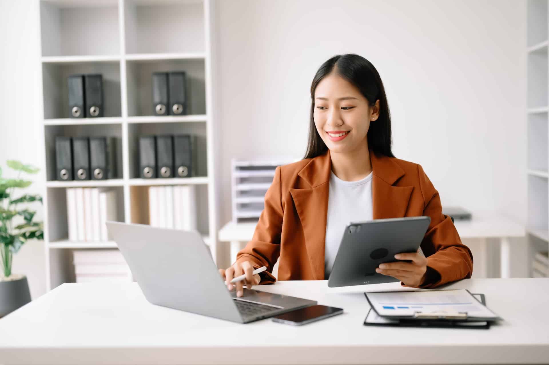 A woman being highly productive and focused, managing her laptop, tablet, and papers to stay immersed in deep work.