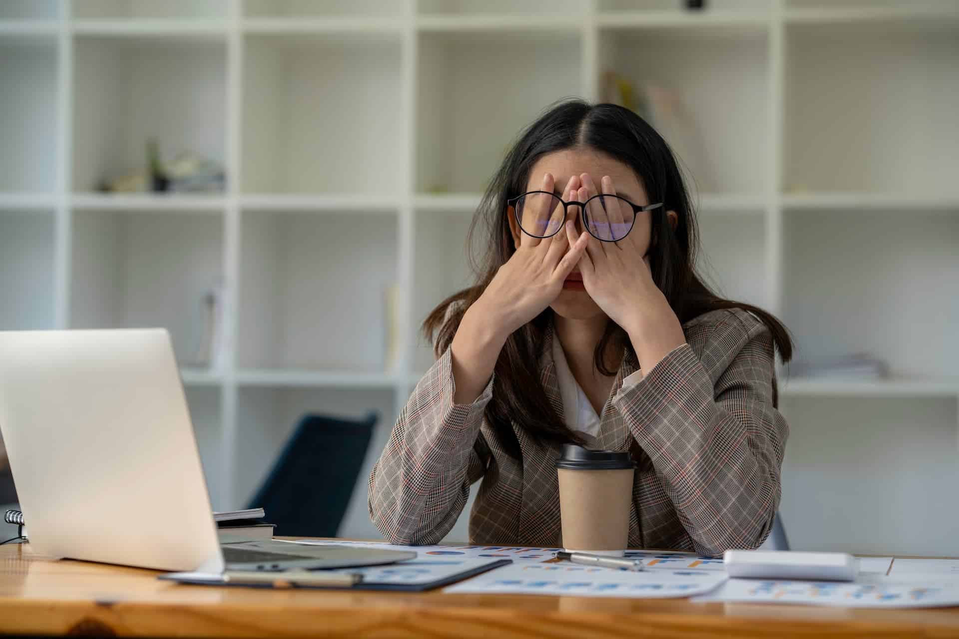 A stressed woman in an office massaging her eyes, highlighting the importance of stress management in the workplace.