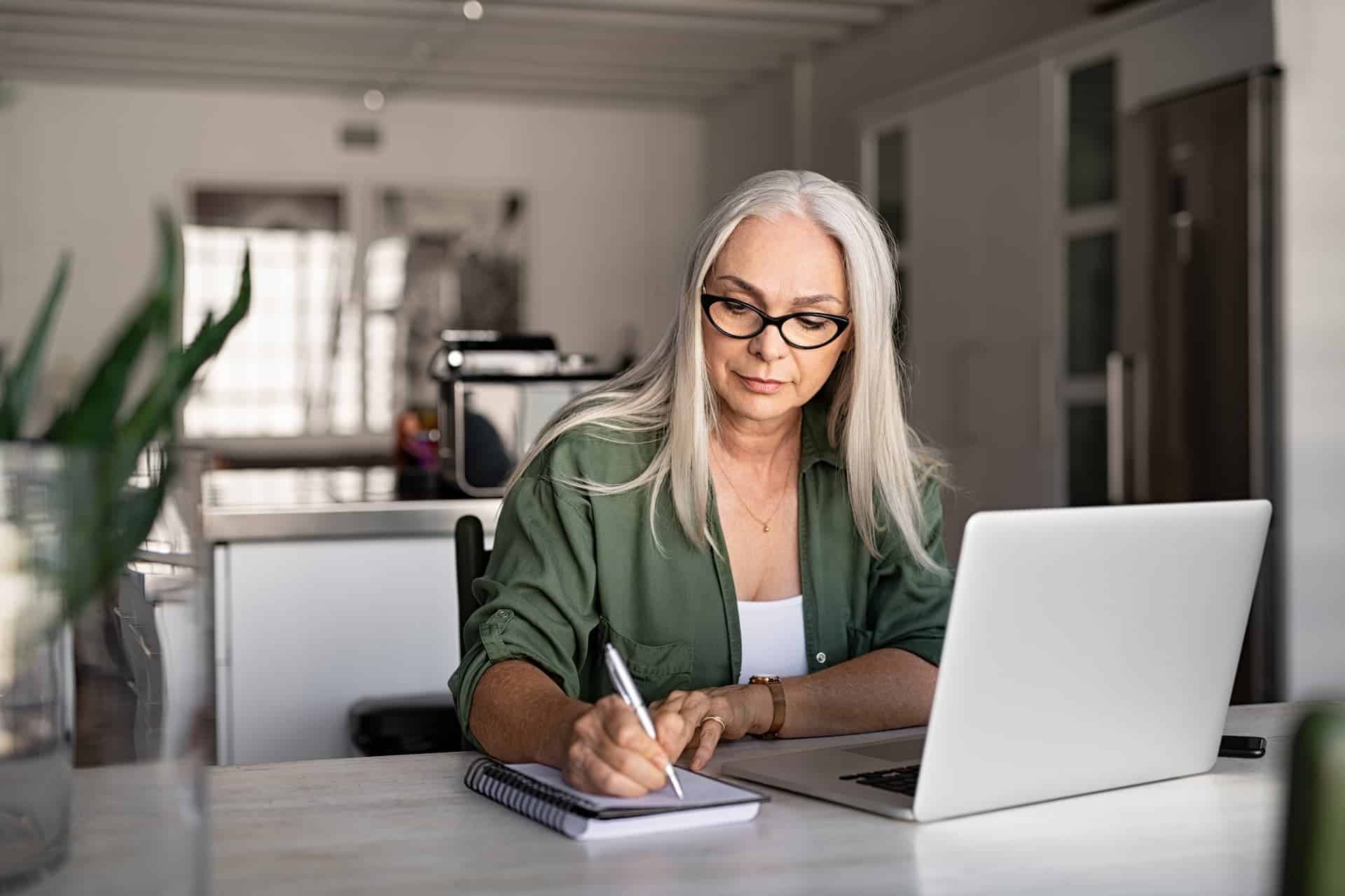 A woman working on her laptop and taking notes, demonstrating deep work and focus to complete her tasks.