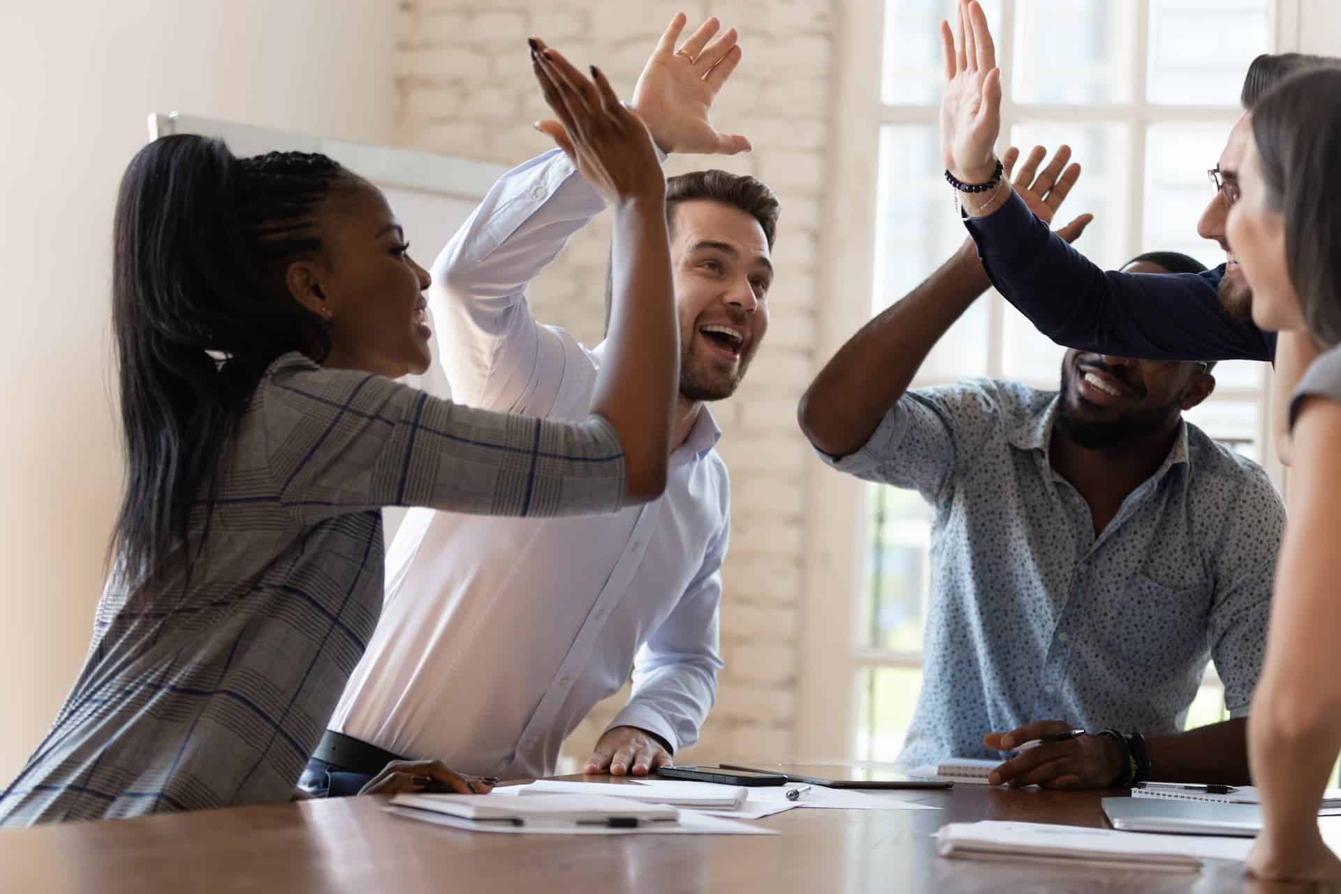 A team celebrating success by high fiving each other at a conference table.