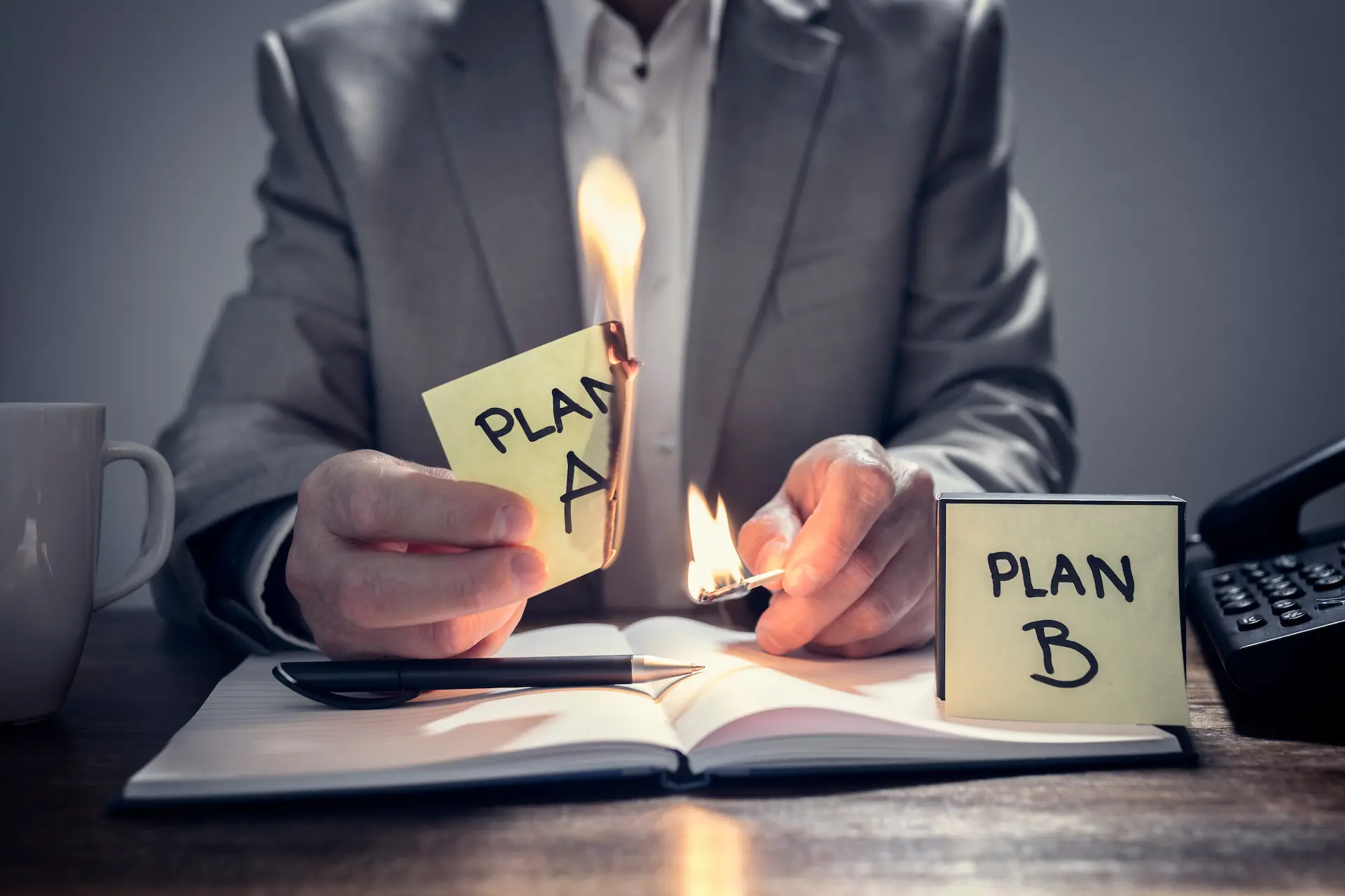 A man holds a burning "Plan A" post-it while revealing "Plan B," symbolizing organizational agility in pivoting strategies effectively.